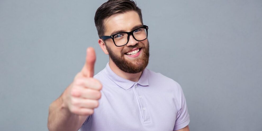 portrait of smiling young man in glasses with beard giving thumbs up