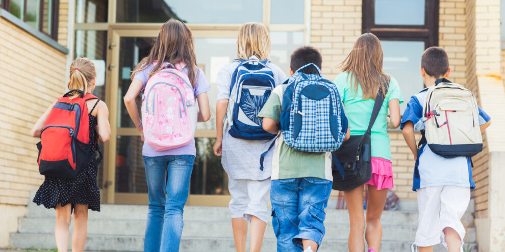 back to school picture of multiple kids walking into school with their backpacks