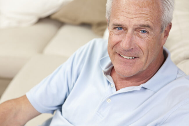 Happy and healthy senior man sitting on a sofa at home smiling and happy