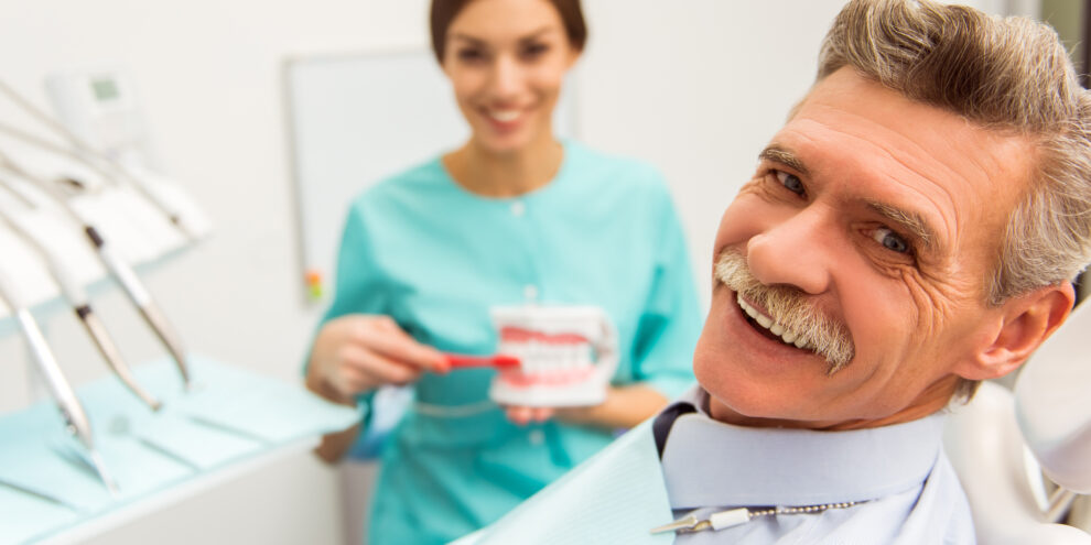 Elderly man and dentist holding a model of dentures smiling