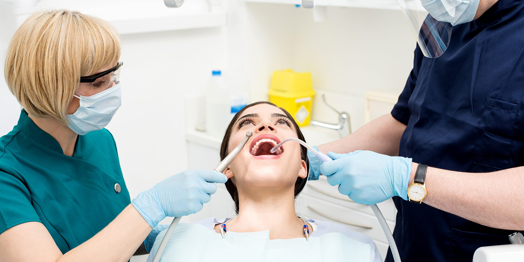 Male dentist treating patient teeth with assistant for routine dental cleaning
