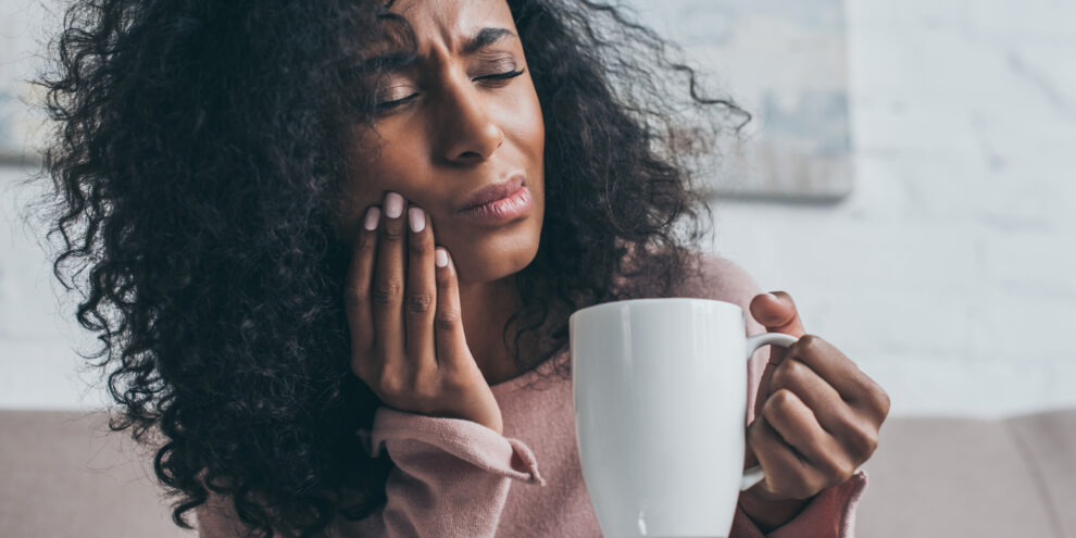 woman holding cheek with dental pain (which is a dental emergency)