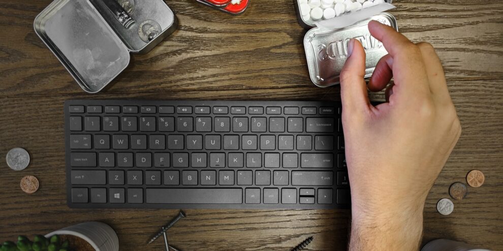 man's hand grabbing a mint from container reaching over his keyboard and desk