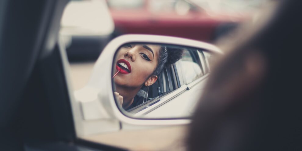 woman looking at her teeth in a car mirror