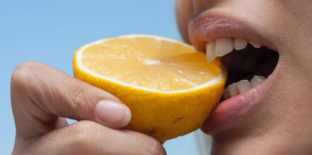 woman biting acidic lemon which can cause yellow teeth