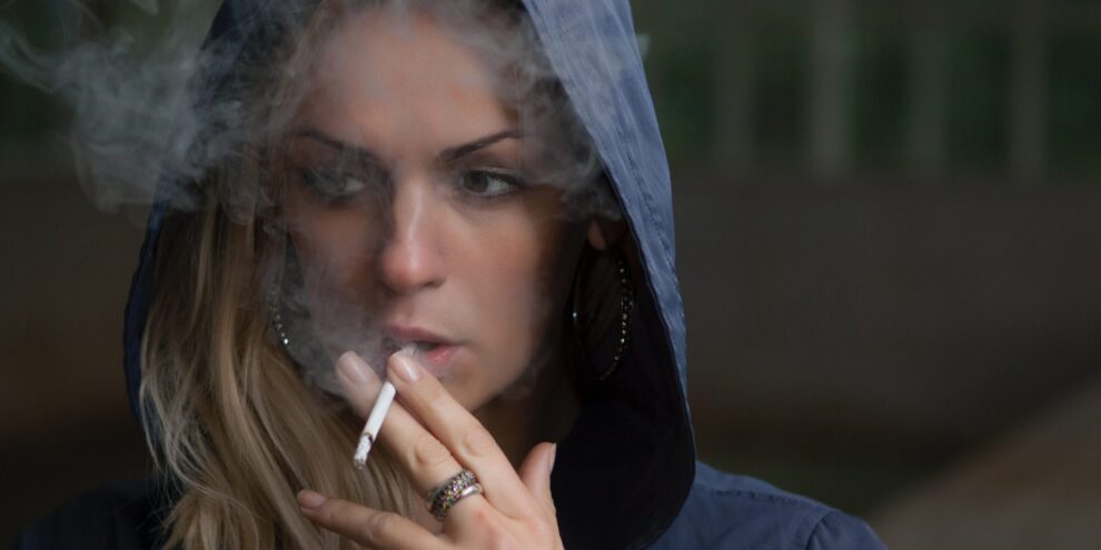 A woman smokes a cigarette, which indicates the origin of her bad breath