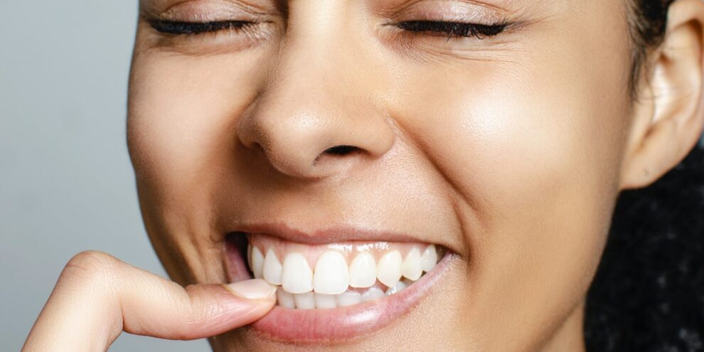 black woman smiling and touching her teeth after teeth whitening treatment