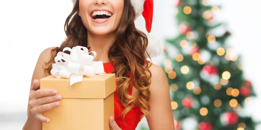 woman in red dress with santa hat holding a present in front of a christmas tree