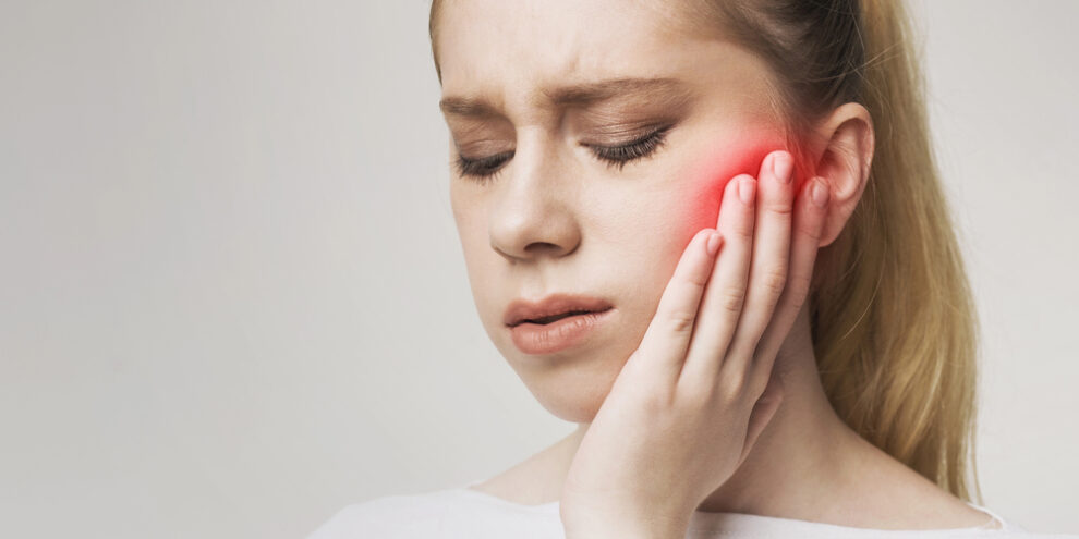 woman with tooth pain, red spot on face, covering side of face with hand