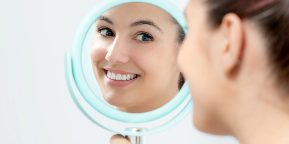 woman smiling in a round mirror after visiting a cosmetic dentist