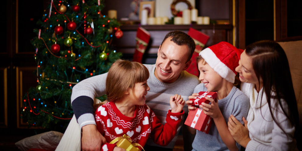 happy family of four opening presents in front of fire place and Christmas tree