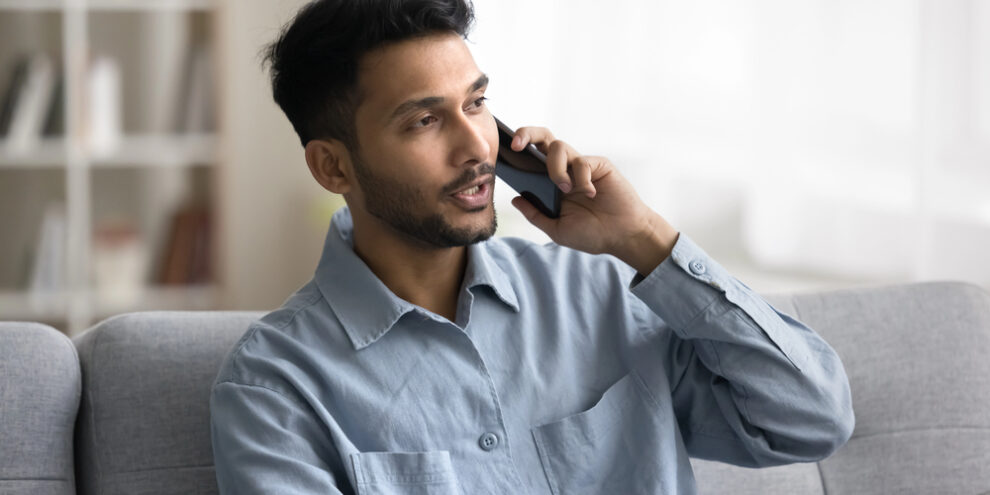 middle-aged Indian man on the phone wearing a blue collared shirt