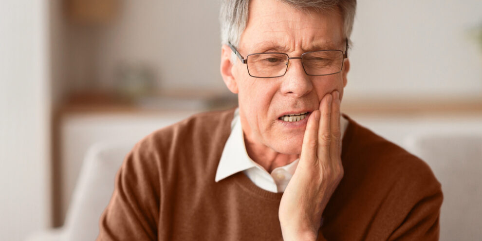 older man wincing and holding his cheek in pain
