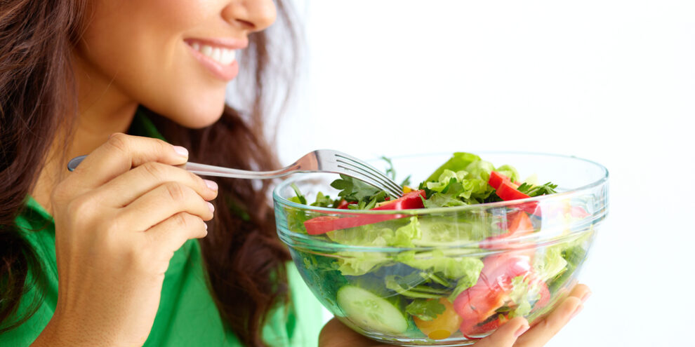 woman using a fork to eat a salad in a clear bowl