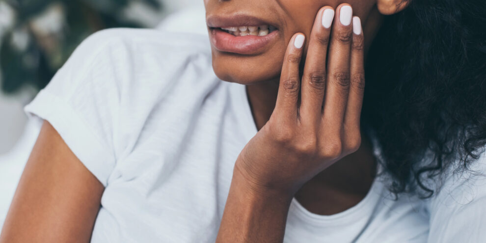 close up of black woman wincing and touching the side of her face because of tooth pain