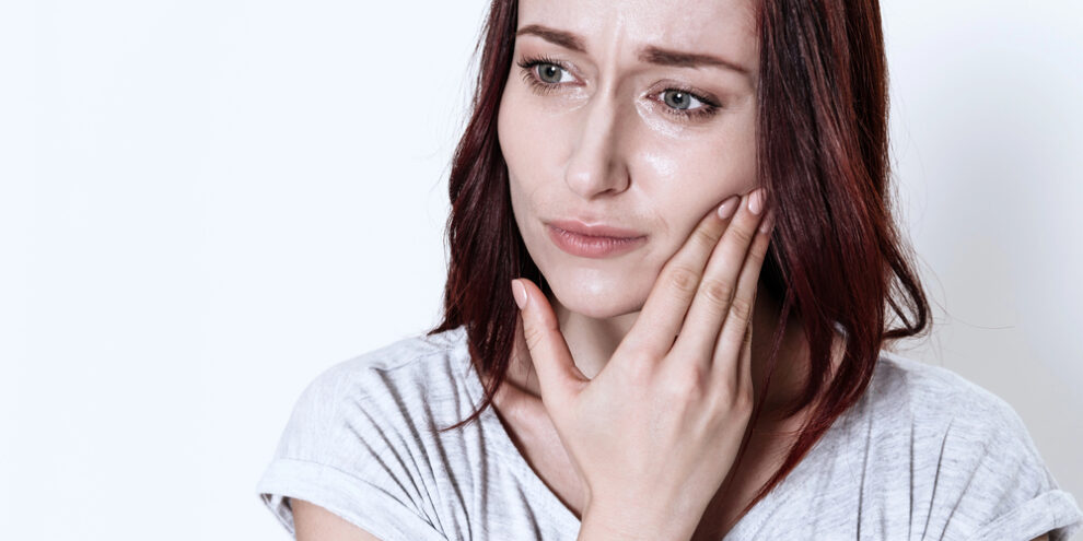 younger woman with brown hair touching her jaw in pain