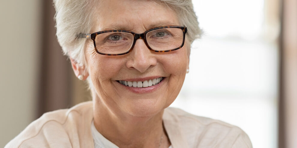 older woman with glasses smiling, wearing a cream-colored cardigan