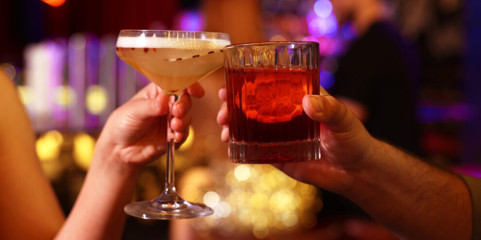 two people clinking their alcoholic beverages together, whiskey and martini