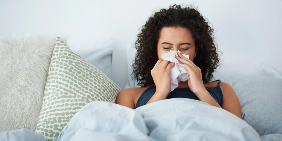 Shot of an attractive young woman feeling sick and blowing her nose while in bed in the morning.