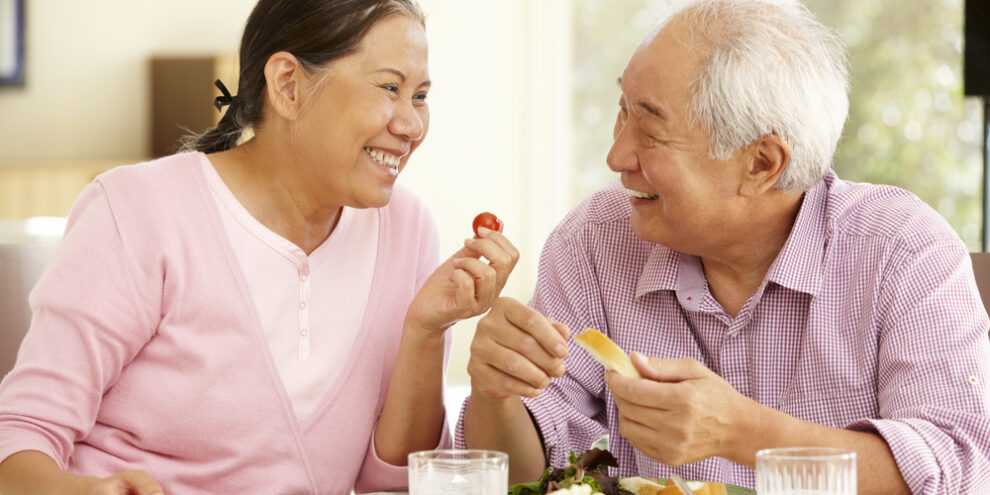 senior couple laughing and sharing a meal together in their home