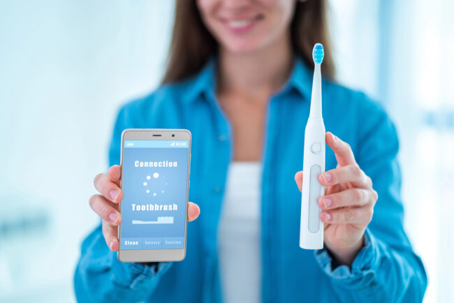 woman holding an electric toothbrush with a phone app